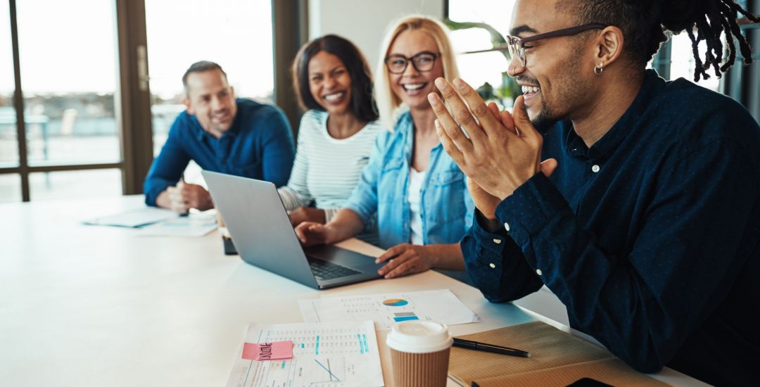 African American office worker laughing with colleagues in a meeting Young African American office worker laughing while sitting with a group of diverse colleagues during a meeting